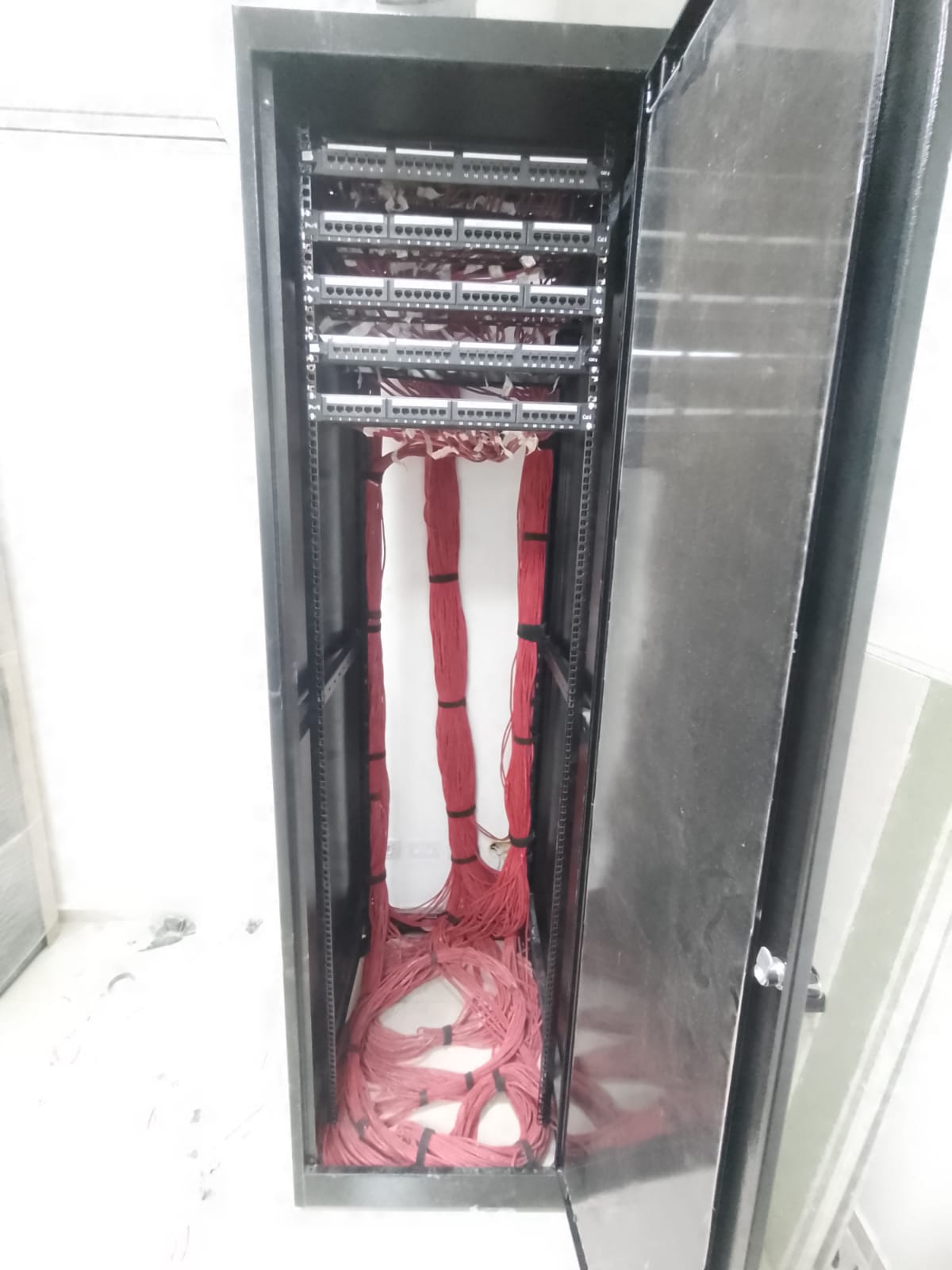 Rack de rede com patch panels e cabeamento estruturado vermelho organizado — projeto finalizado pela CI Tecnologia no estúdio Podpah