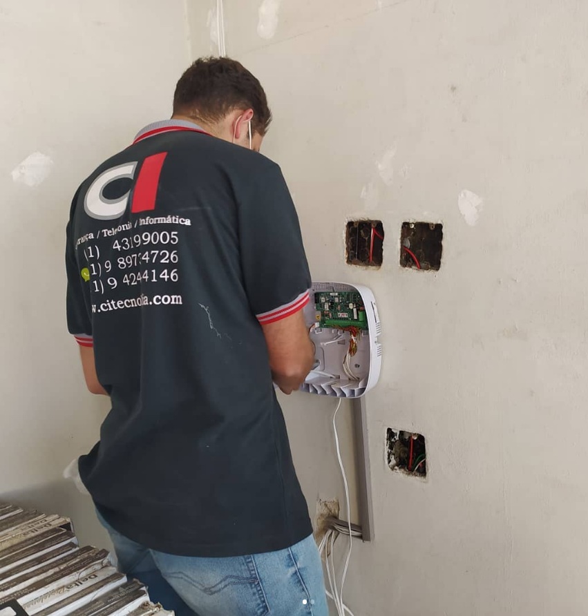 Técnico com uniforme CI Tecnologia instalando equipamento de rede na parede