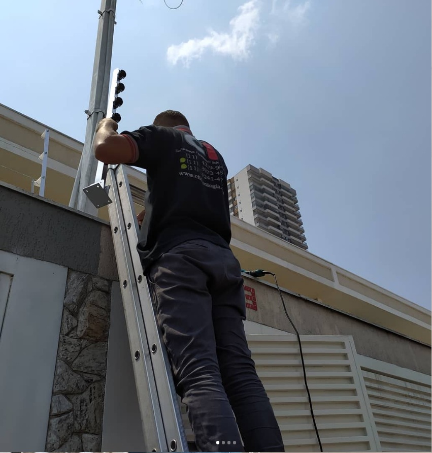 Técnico com uniforme CI Tecnologia em escada instalando infraestrutura de rede externa